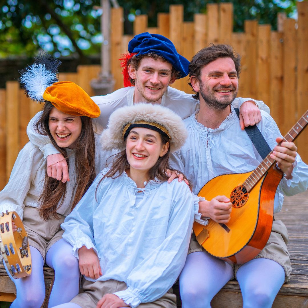 Four people holding medieval instruments and wearing medieval costumes smiling together as a group