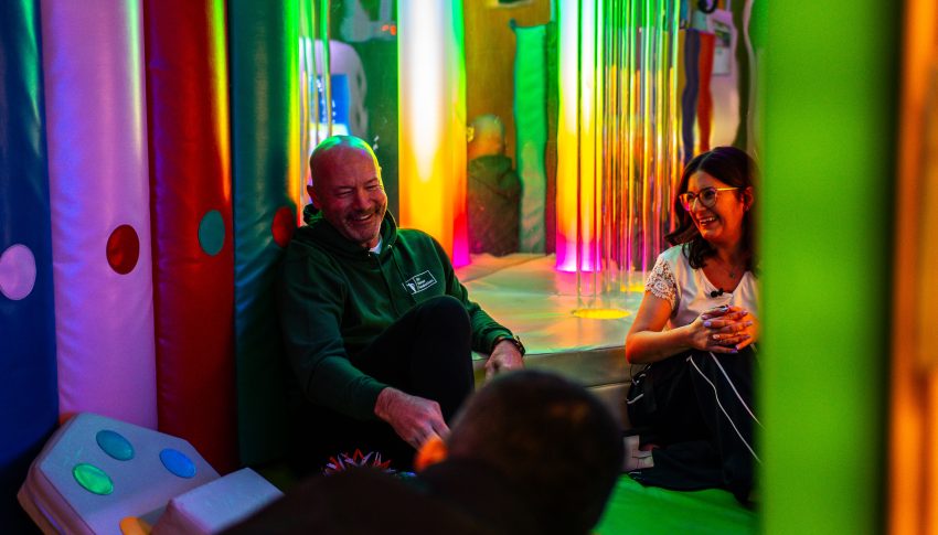 Alan Shearer and and another person sat in a colourful play area in at the Alan Shearer Centre