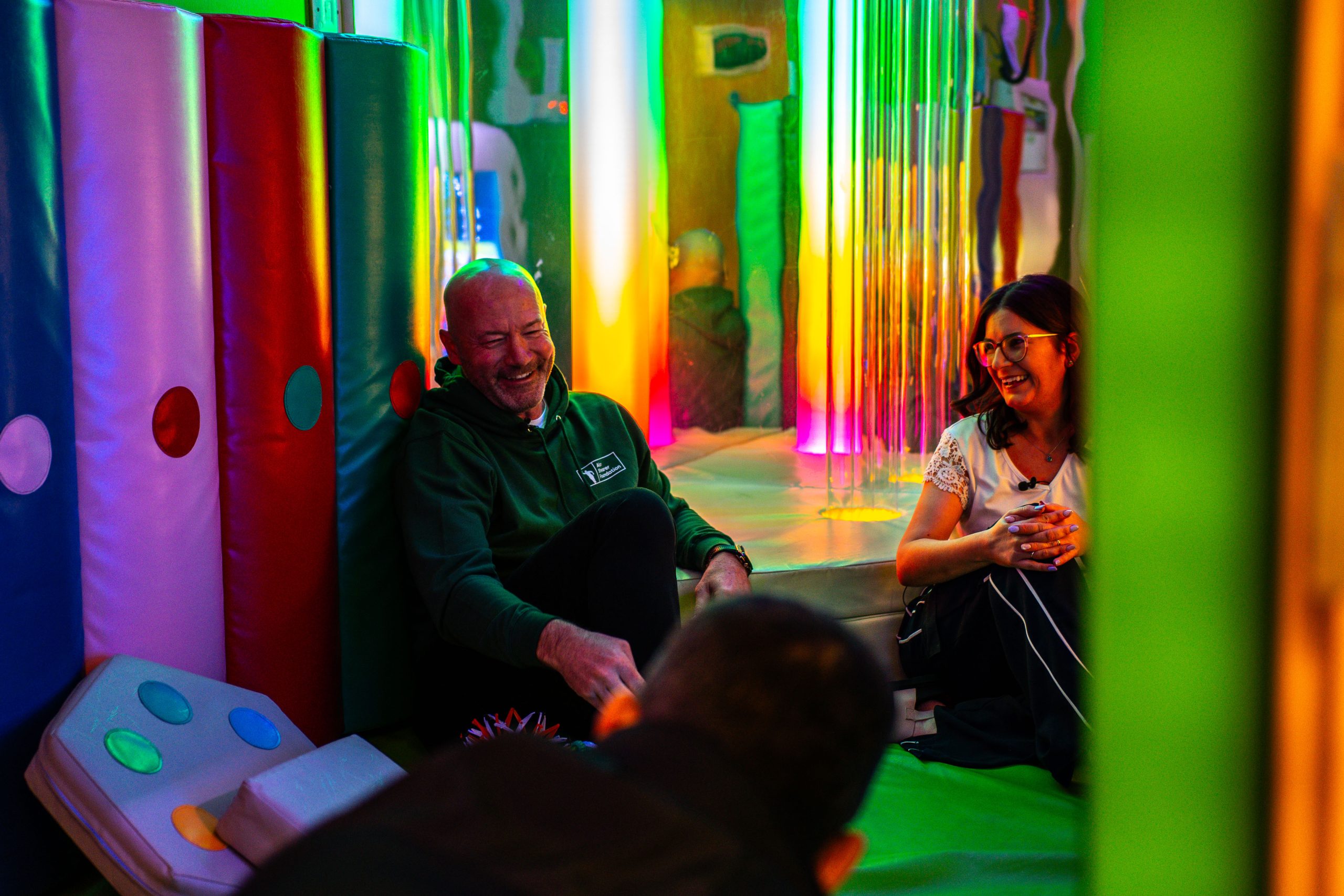 Alan Shearer and and another person sat in a colourful play area in at the Alan Shearer Centre
