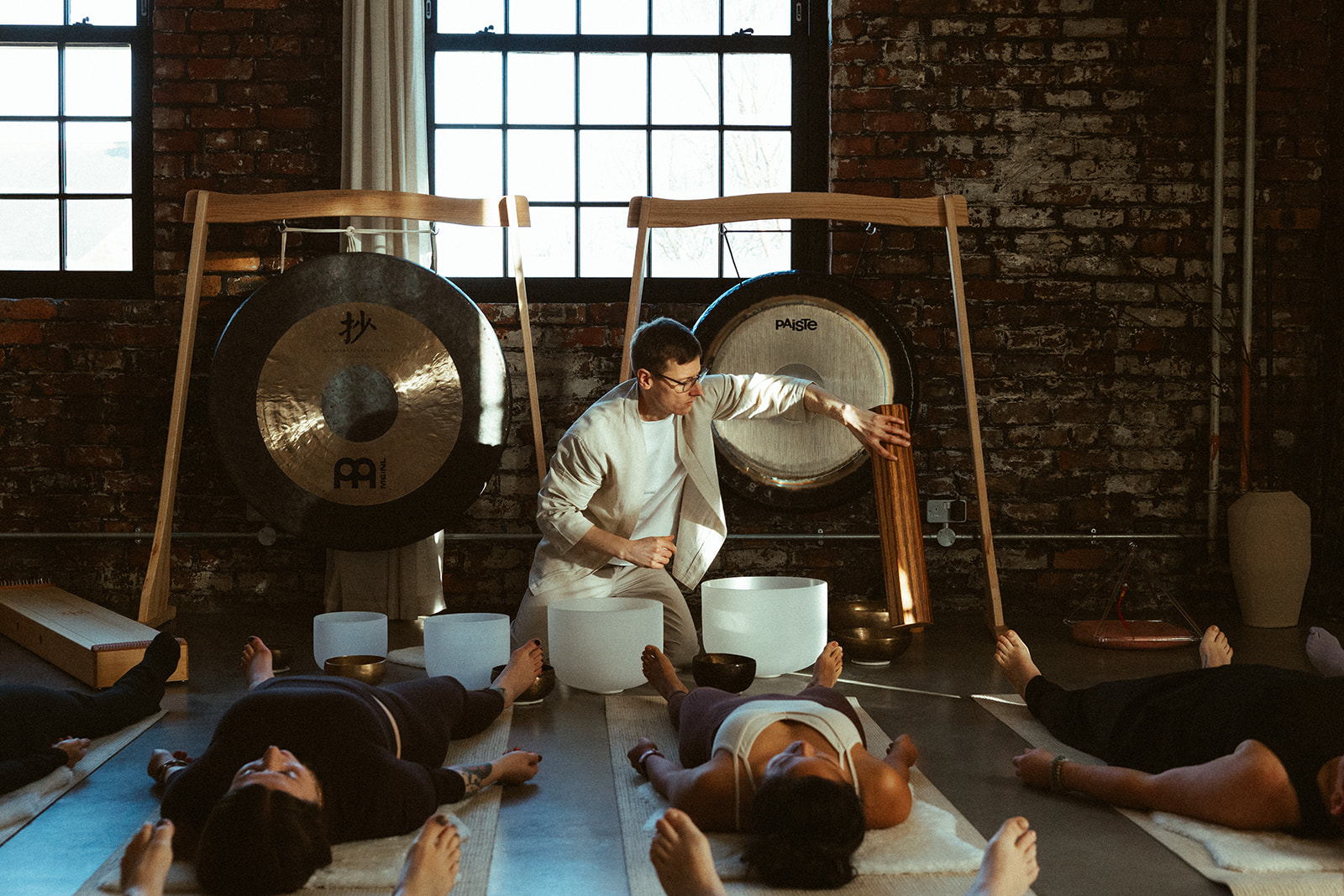 Leader of breathwork class sat at front of room surrounded by sound instruments and attendees lying on mats