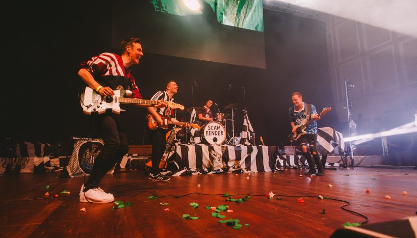 Rock band playing on stage all wearing black and white Newcastle United football tops