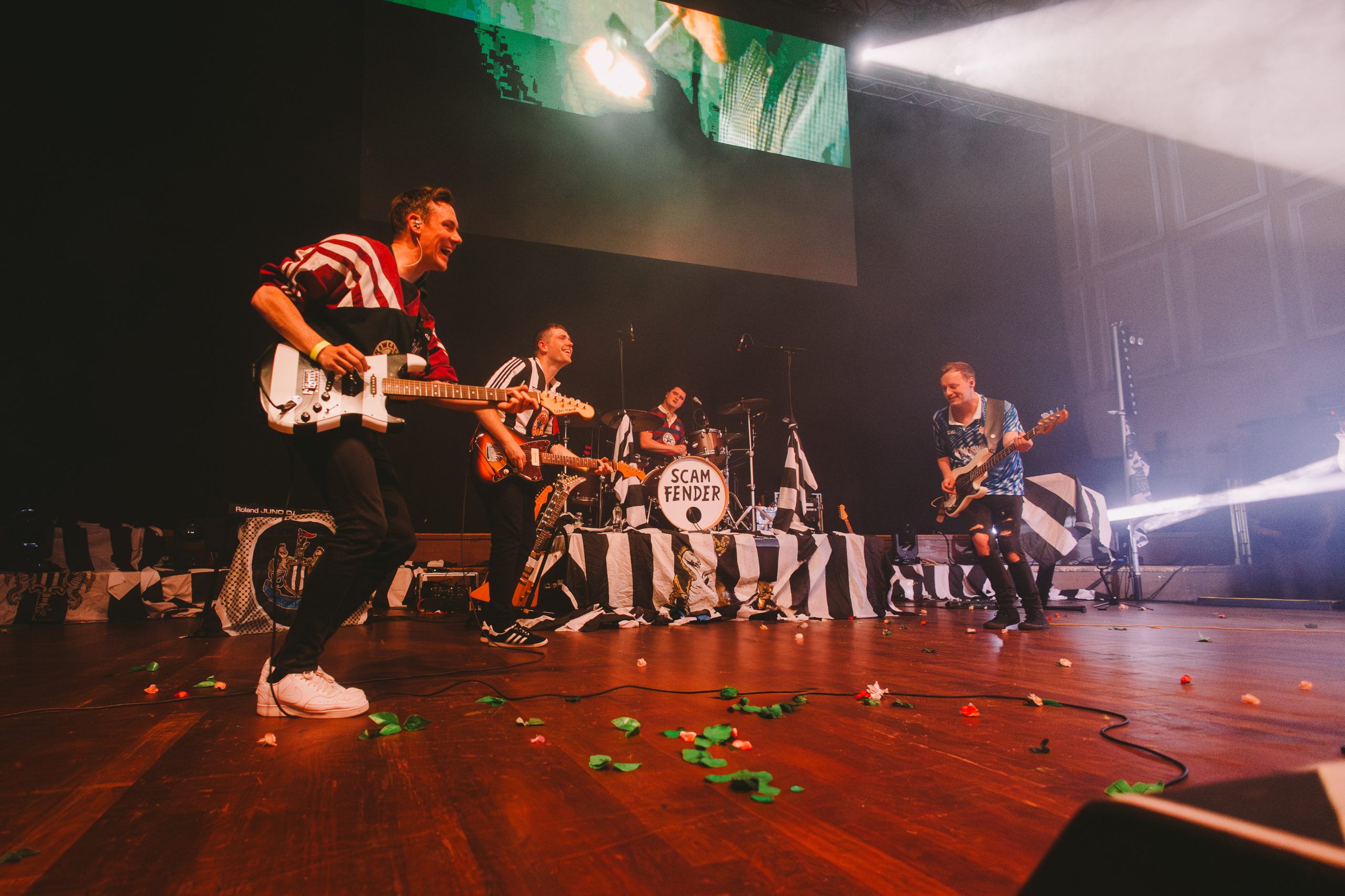 Rock band playing on stage all wearing black and white Newcastle United football tops
