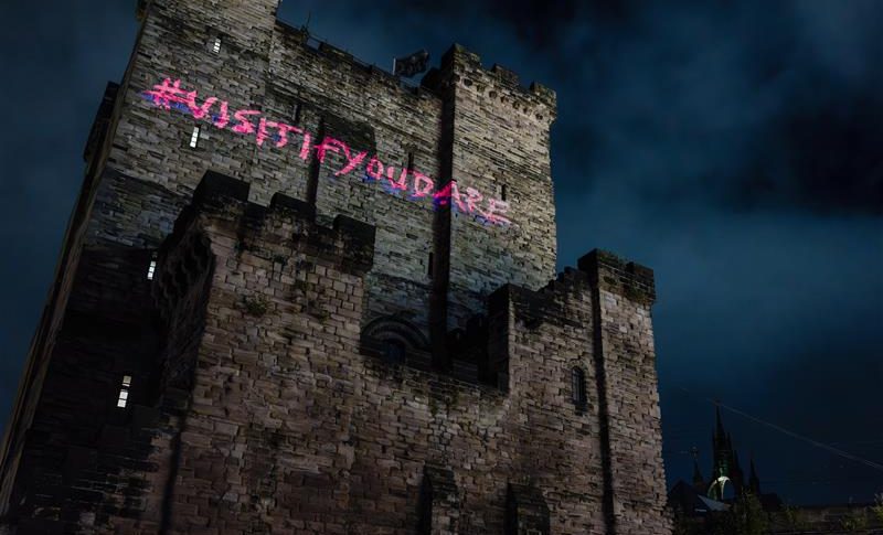 Newcastle Castle Keep at dark with #VisitIfYouDare in pink writing projected onto the side of the building