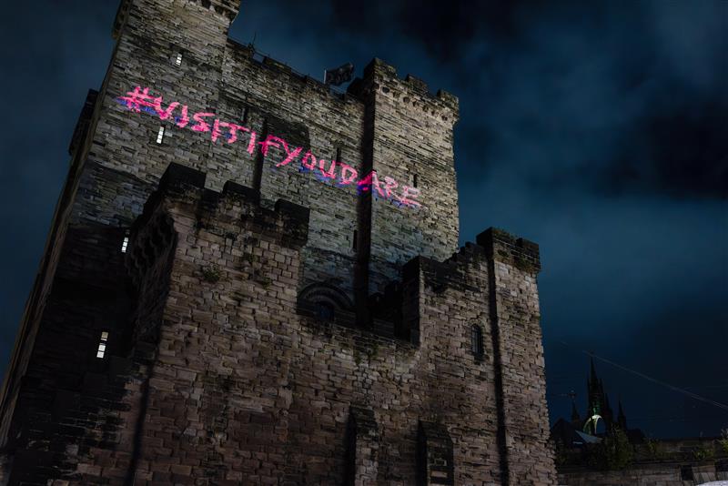 Newcastle Castle Keep at dark with #VisitIfYouDare in pink writing projected onto the side of the building
