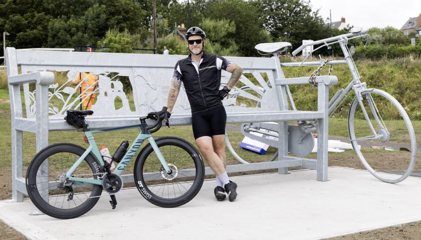 Person in cycling attire and with road bike stood next to new installation.