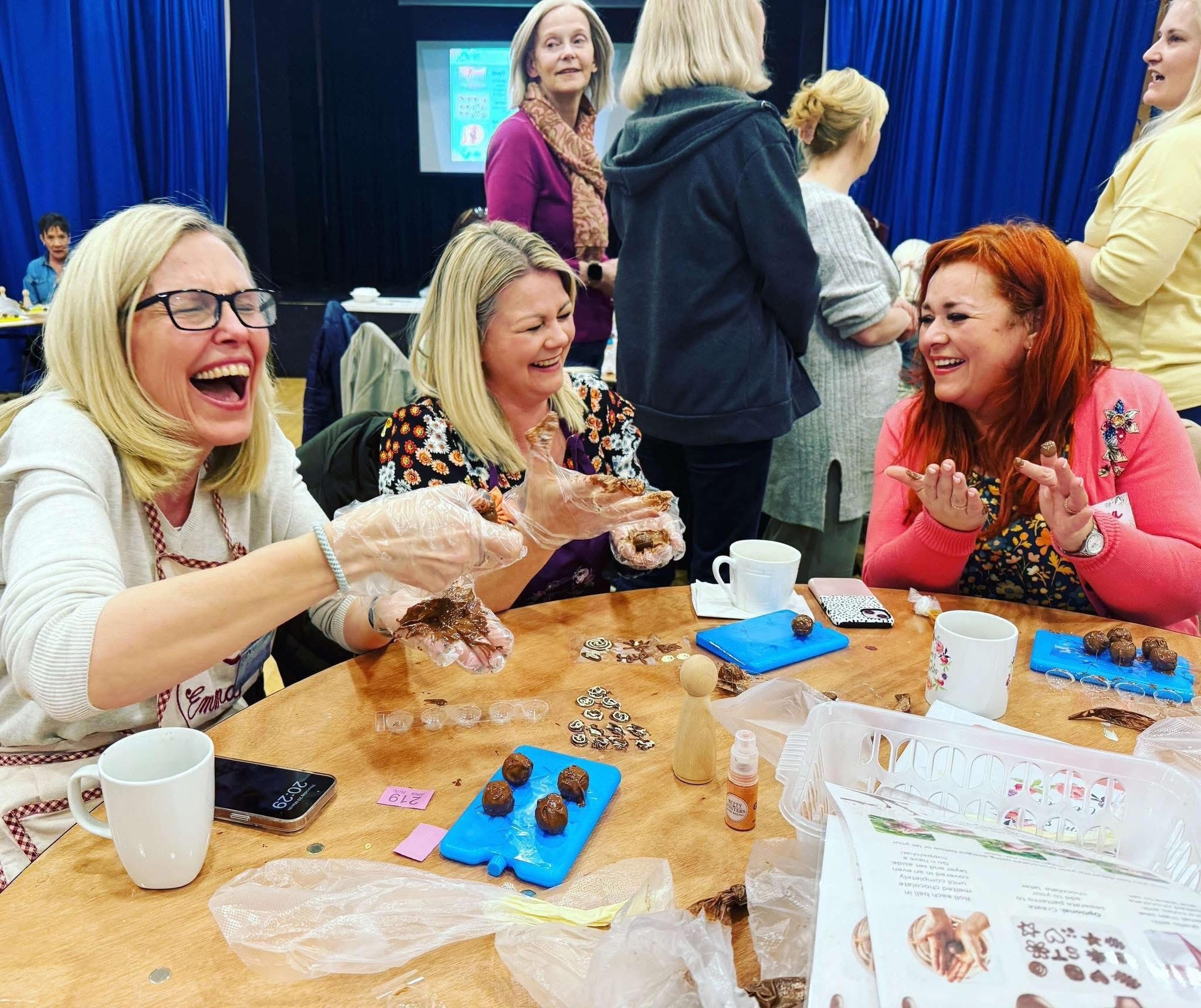 Three people sat around a table making chocolates and laughing hard.
