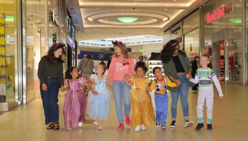 Group of adults and children (who are dressed up as Disney characters) walking through Eldon Square together
