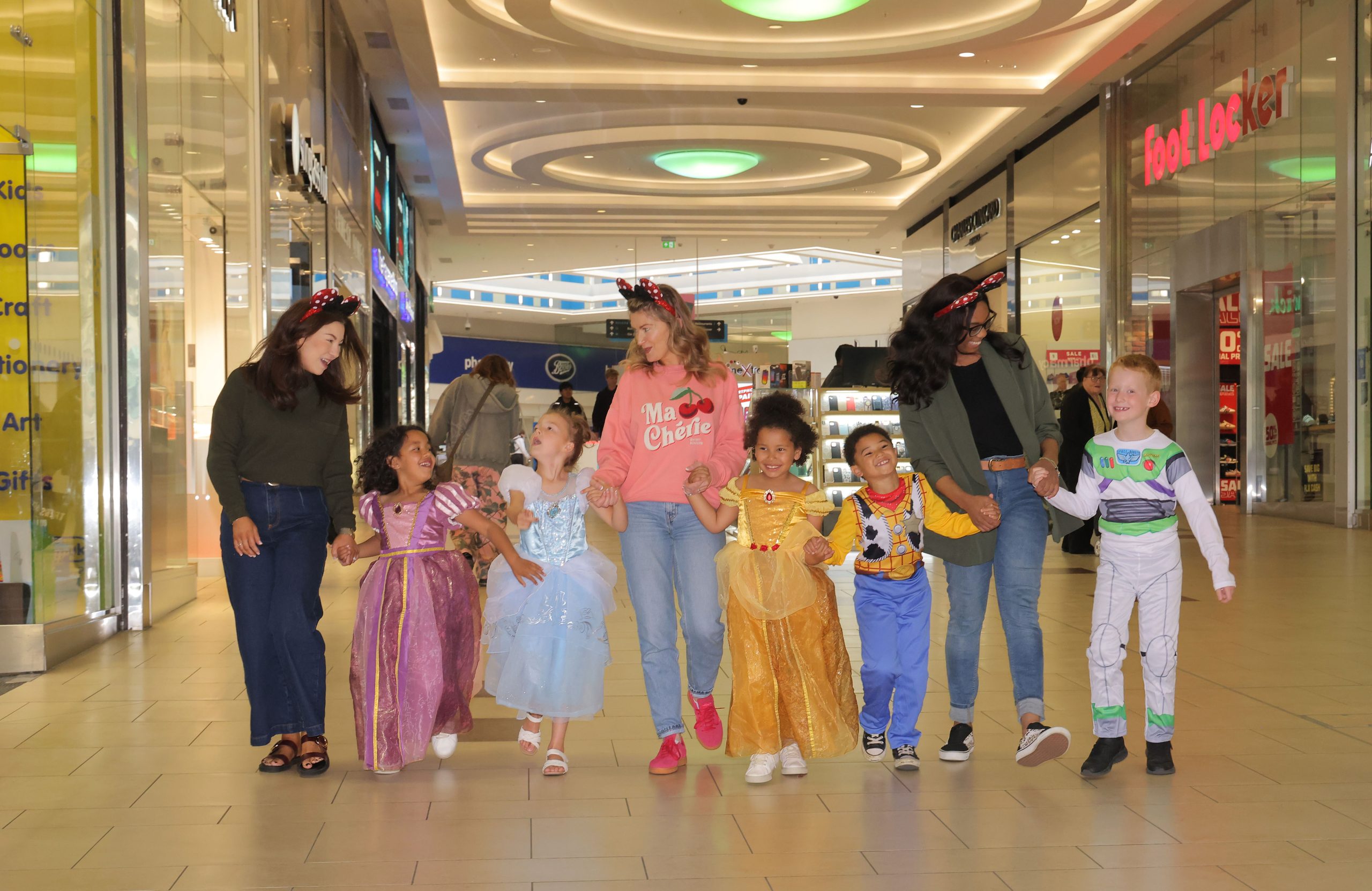 Group of adults and children (who are dressed up as Disney characters) walking through Eldon Square together