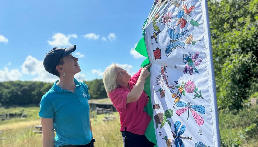 Two people lookinhg at an arty flag at WWT in the bright sunshine.