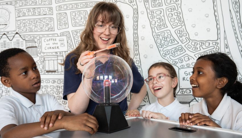 Adult working on a science experiment with three children looking on in wonder.