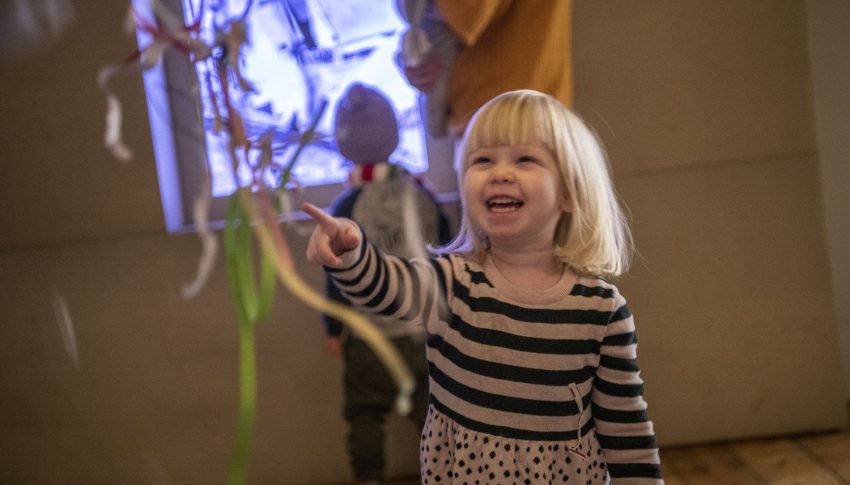 Child laughing as they look and point at a sculpture.