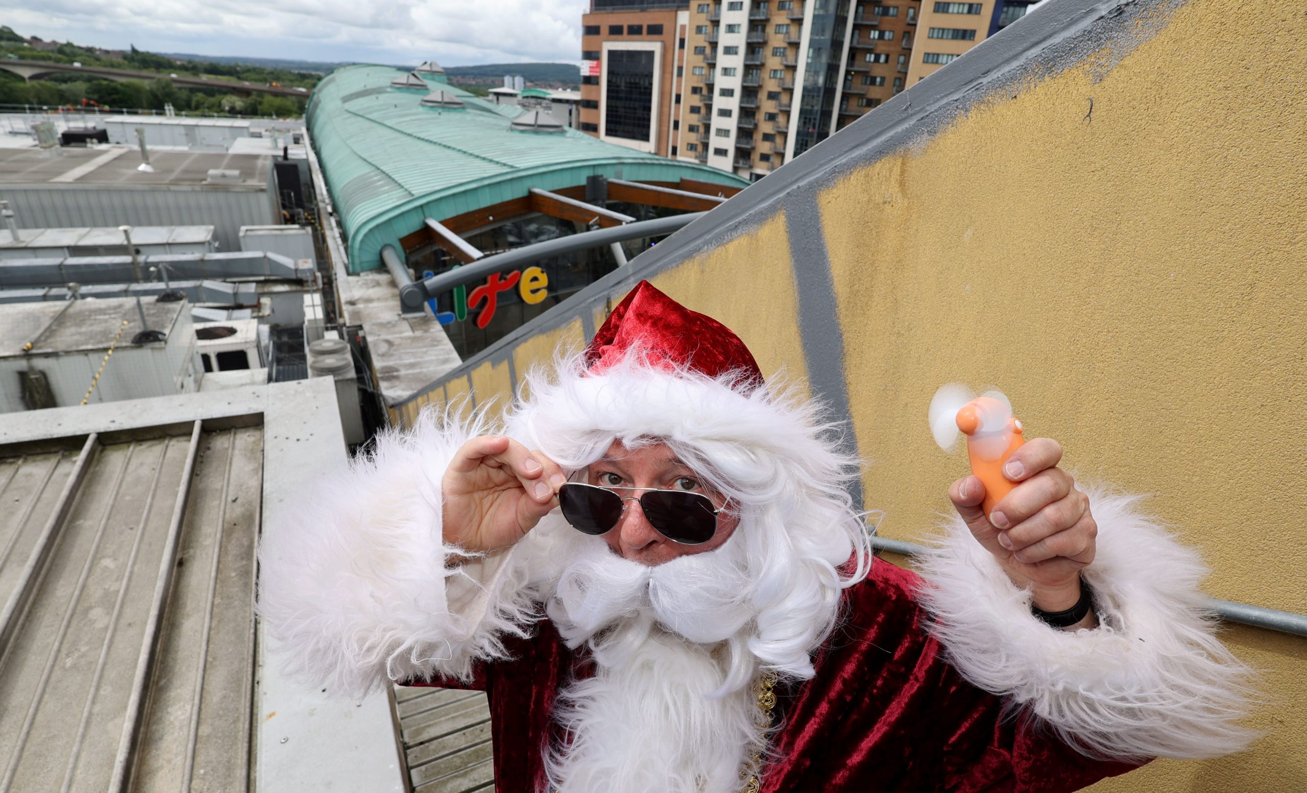 Santa holding an electric hand-held fan on top of Centre for Life's roof