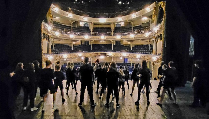 Students performing on stage at Tyne Theatre & Opera House. The image is taken from the back of the stage out towards the audience.