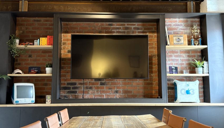 View of the Cargo boardroom with a tv in the middle of the wall which is open brick with shelving and nic-knacks dotted around.