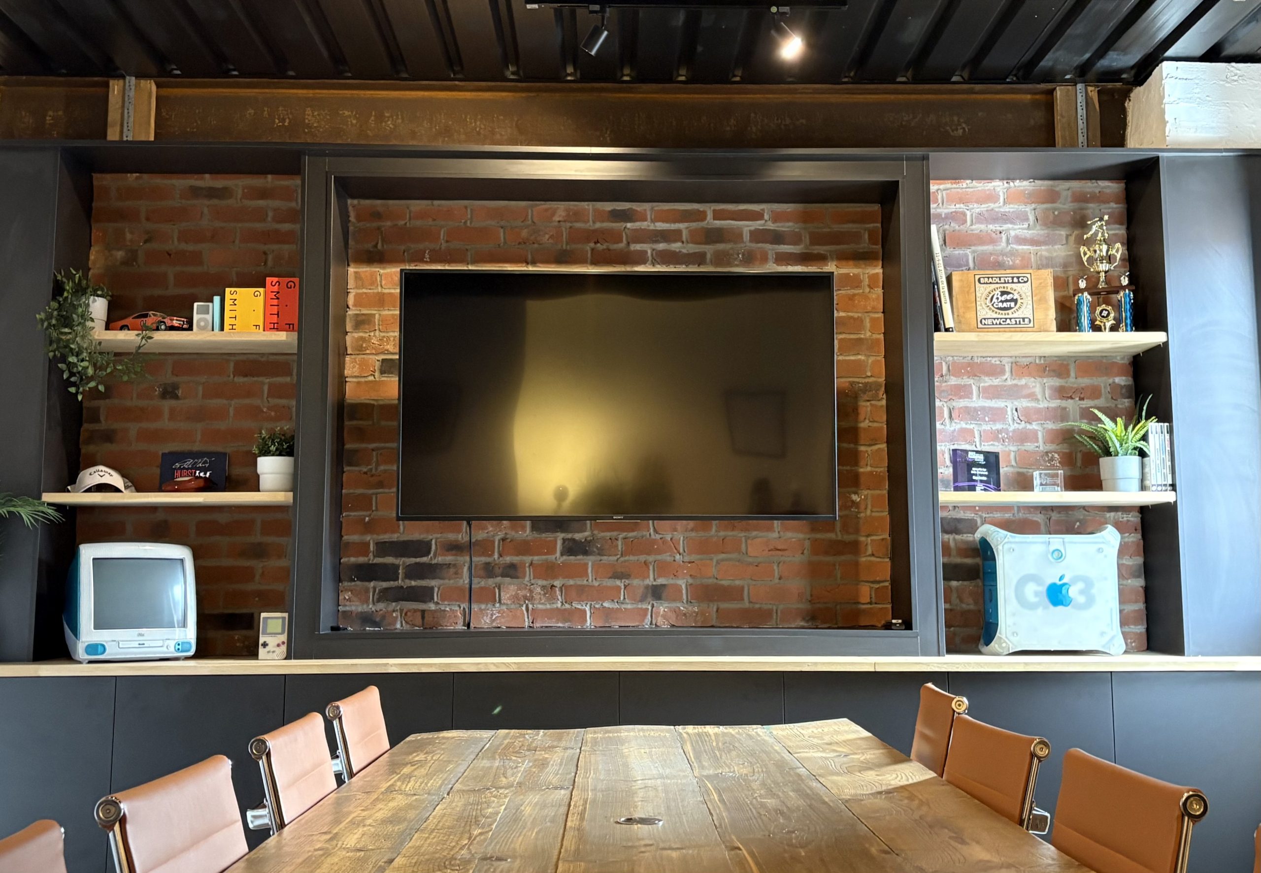 View of the Cargo boardroom with a tv in the middle of the wall which is open brick with shelving and nic-knacks dotted around.