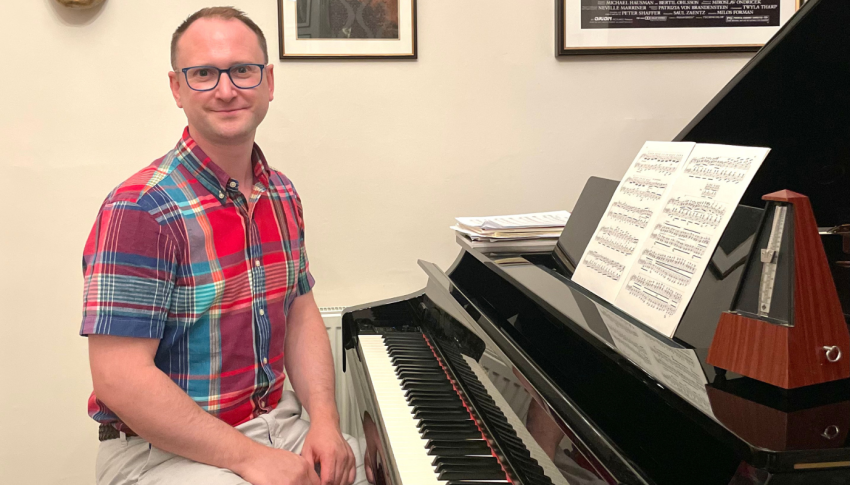 Choir Director sat at a piano forte smiling to camera.
