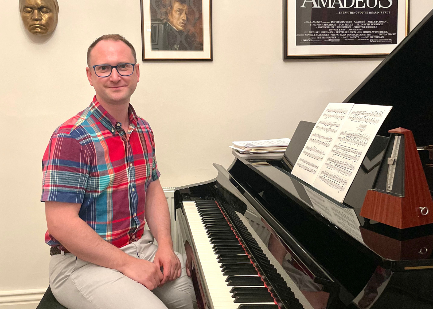 Choir Director sat at a piano forte smiling to camera.