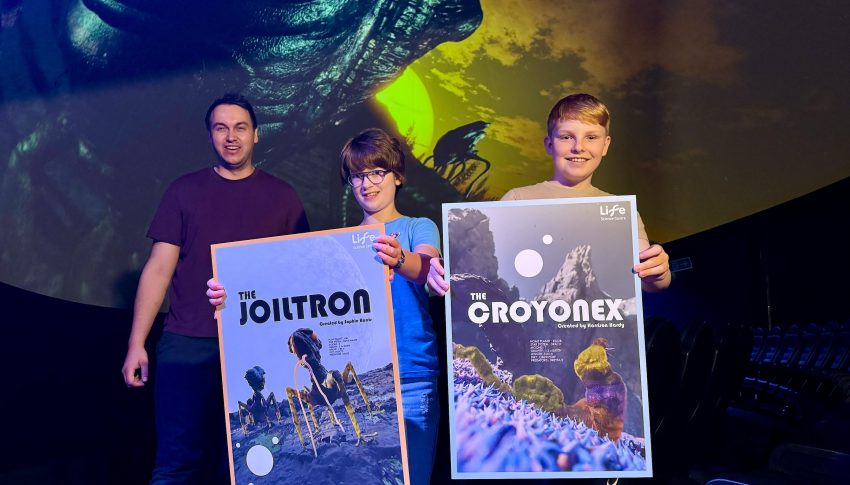 Two young winners of competition and staff member of Life. The children are holding posters with their aliens presented on.