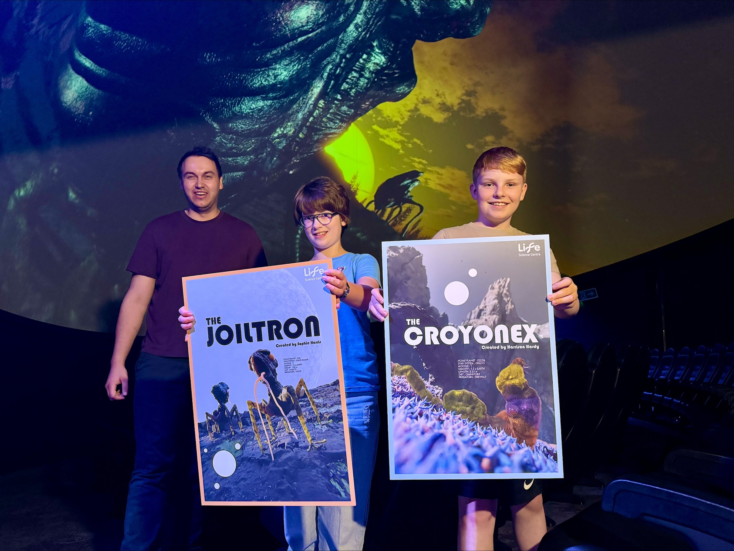 Two young winners of competition and staff member of Life. The children are holding posters with their aliens presented on.