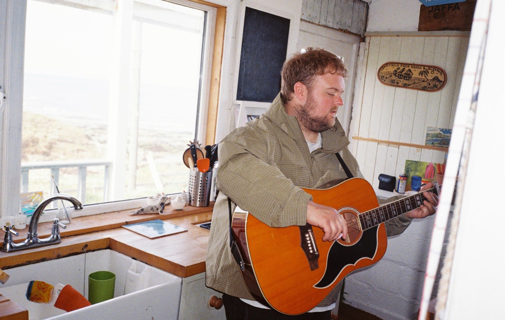 Person stood in a kitchen strumming on an acoustic guitar