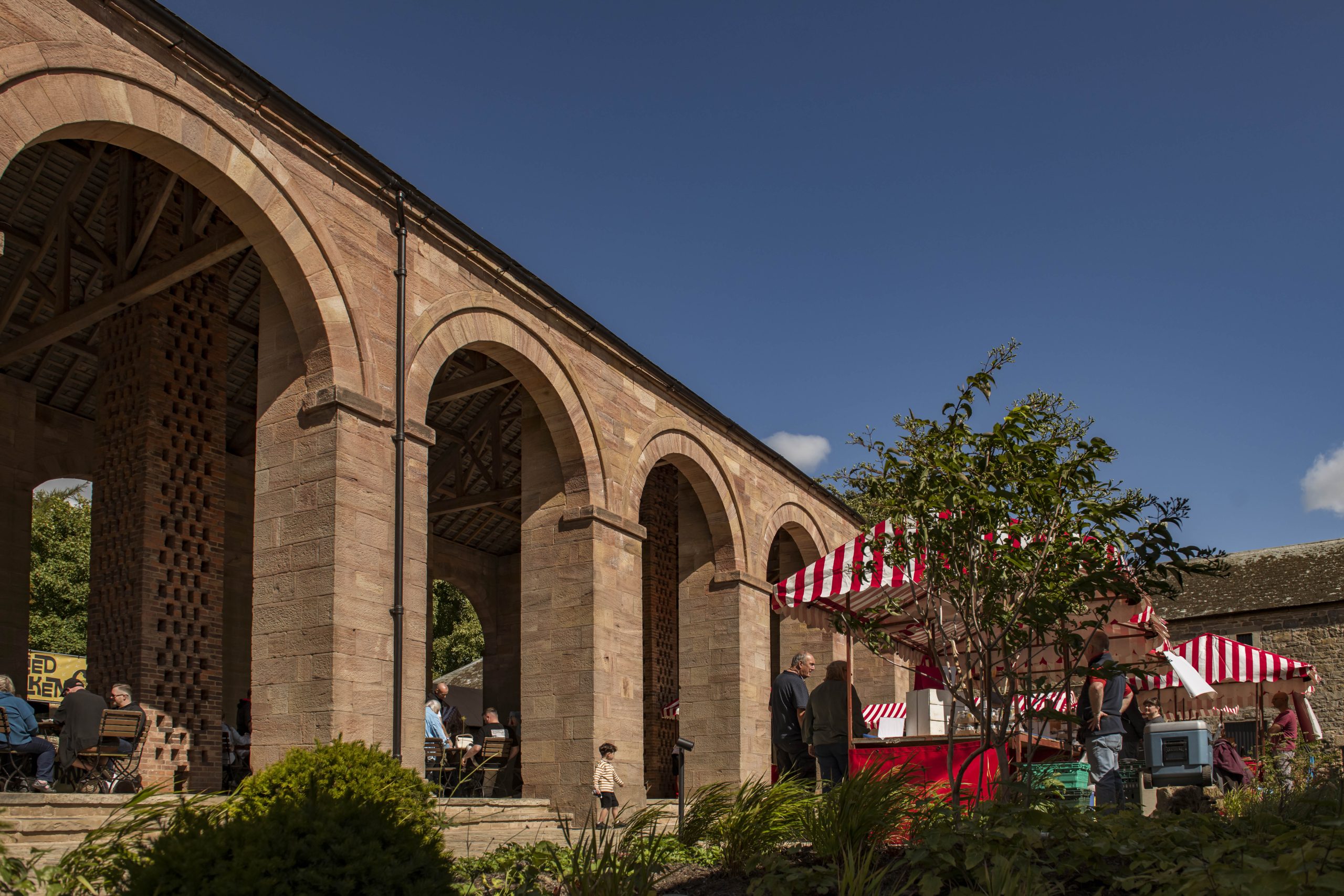 Red and white market stalls outside the arches of the Raby barn.