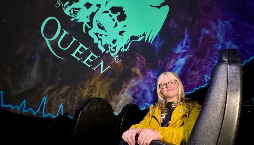 Ruby sat in cinema seat at Centre for Life with 'Queen' logo projected above her.