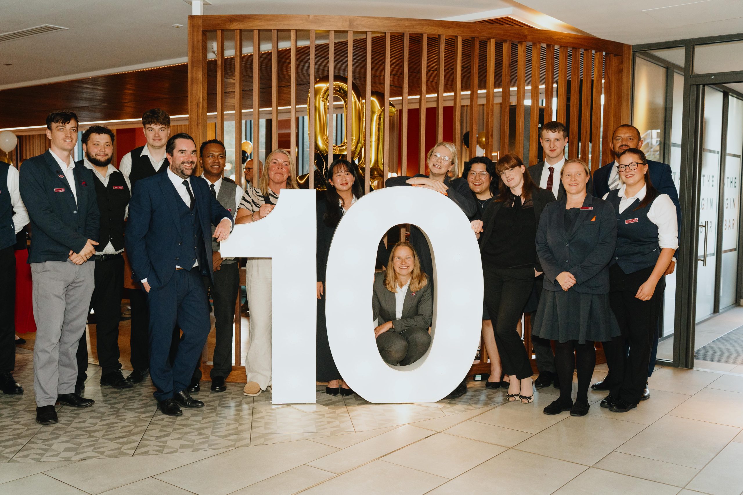 Group of staff from Crowne Plaza stood in lobby together surrounding a large '10' sign.