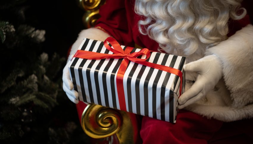Black and white striped gift with ref ribbon tied in a bow, held in the hands of Santa Claus.