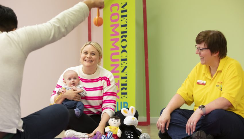 Three people sat crossed legged in a circle, one is holding a baby.