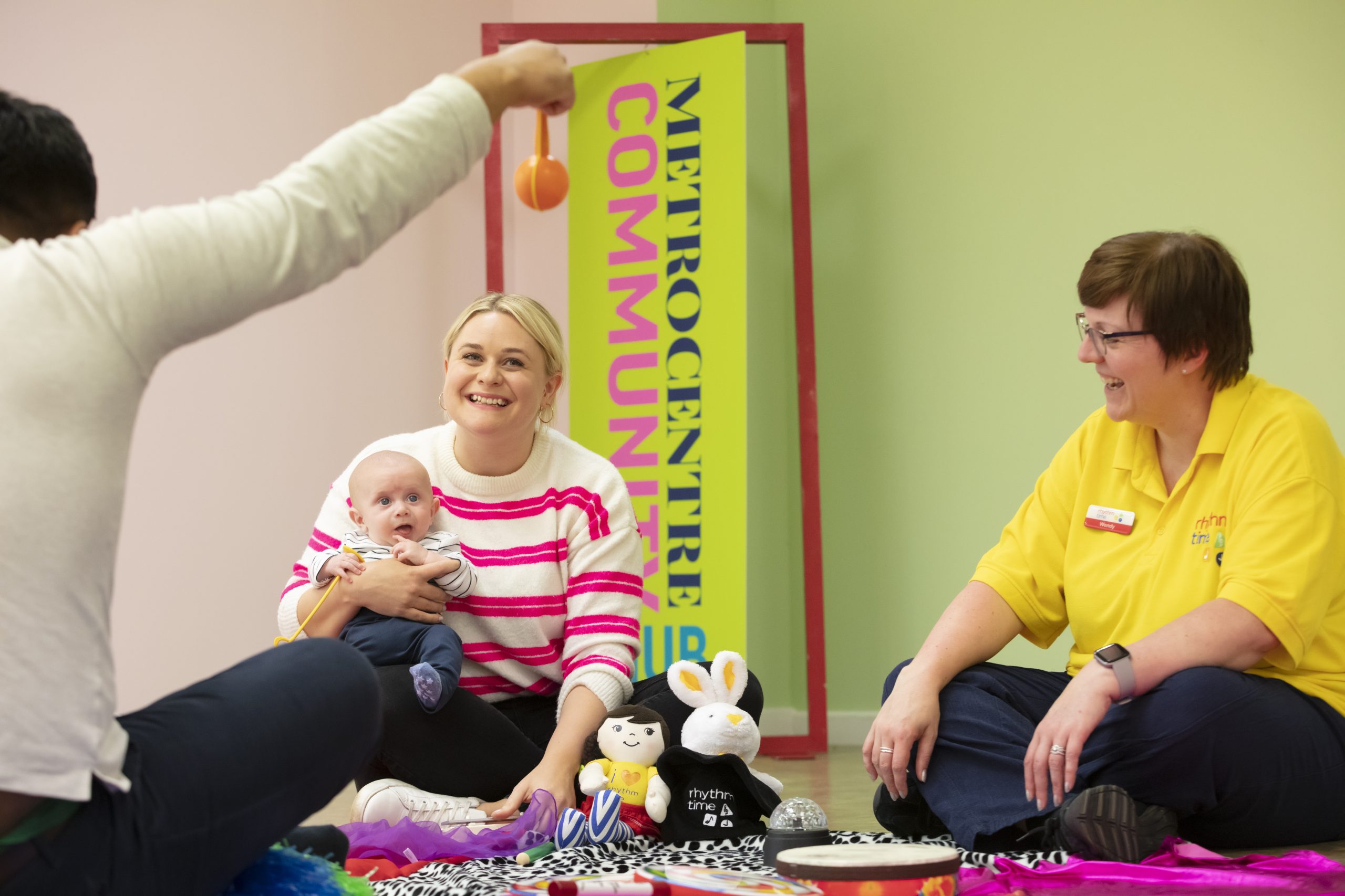 Three people sat crossed legged in a circle, one is holding a baby.
