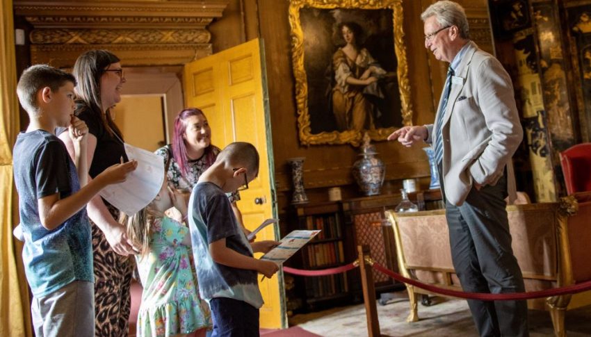 Older person talking to a group of adults and children in a grand state-looking room.