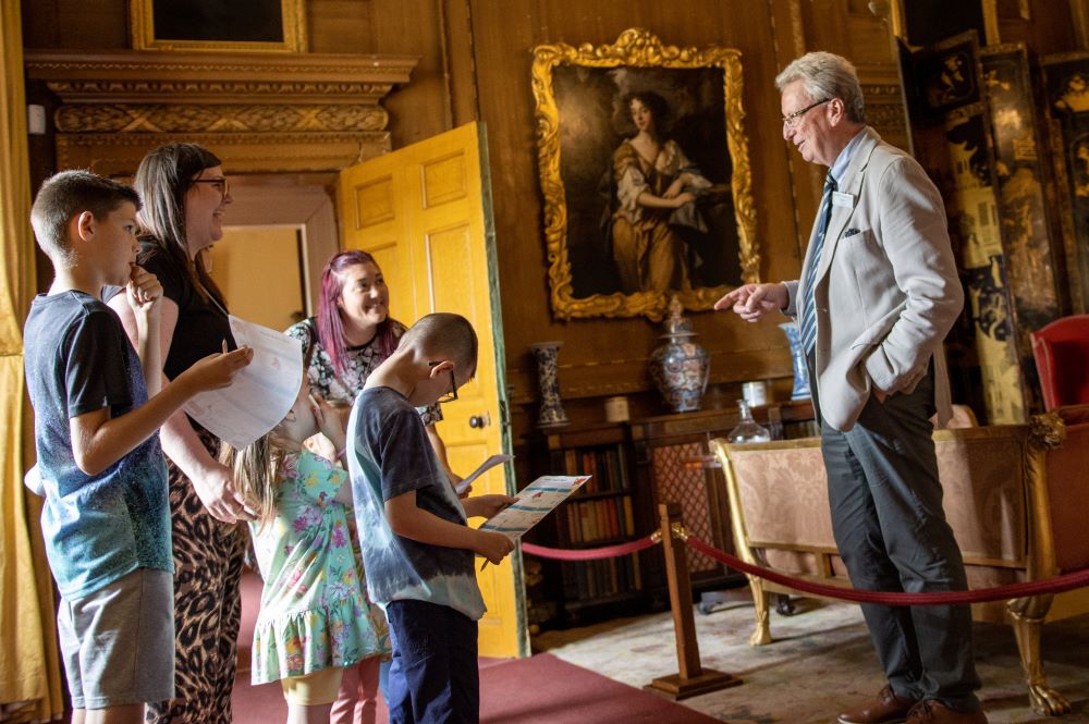 Older person talking to a group of adults and children in a grand state-looking room.