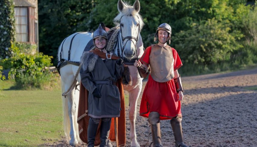 Two women dressed in Medieval costume with a white horse.