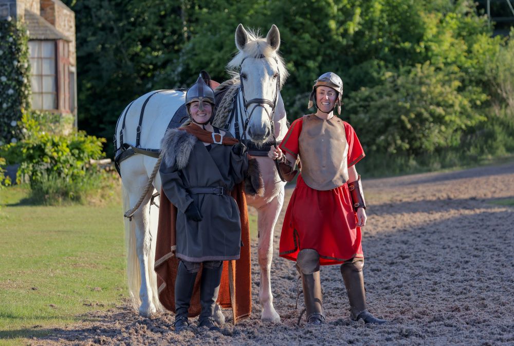 Two women dressed in Medieval costume with a white horse.