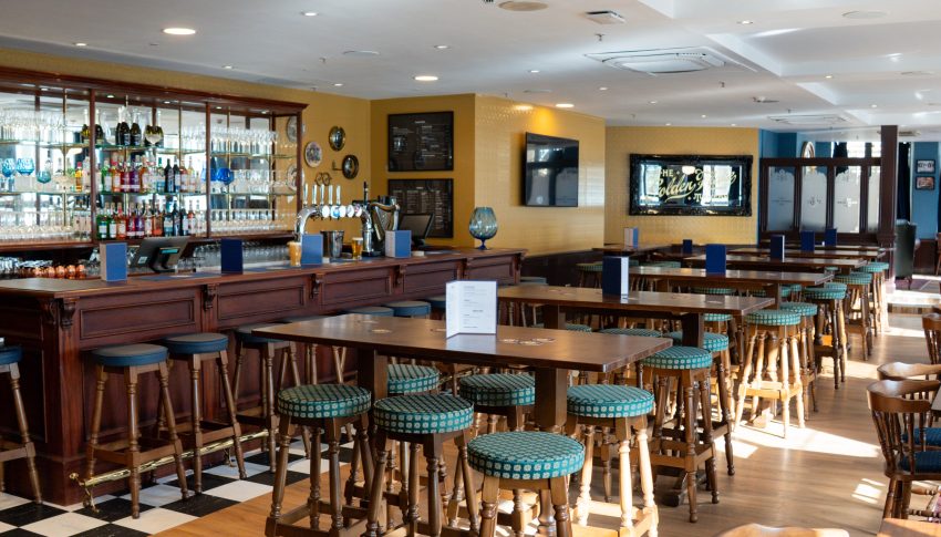 Pub-style room with bar on the left-hand wall and tall tables and tall stools lined across the room.