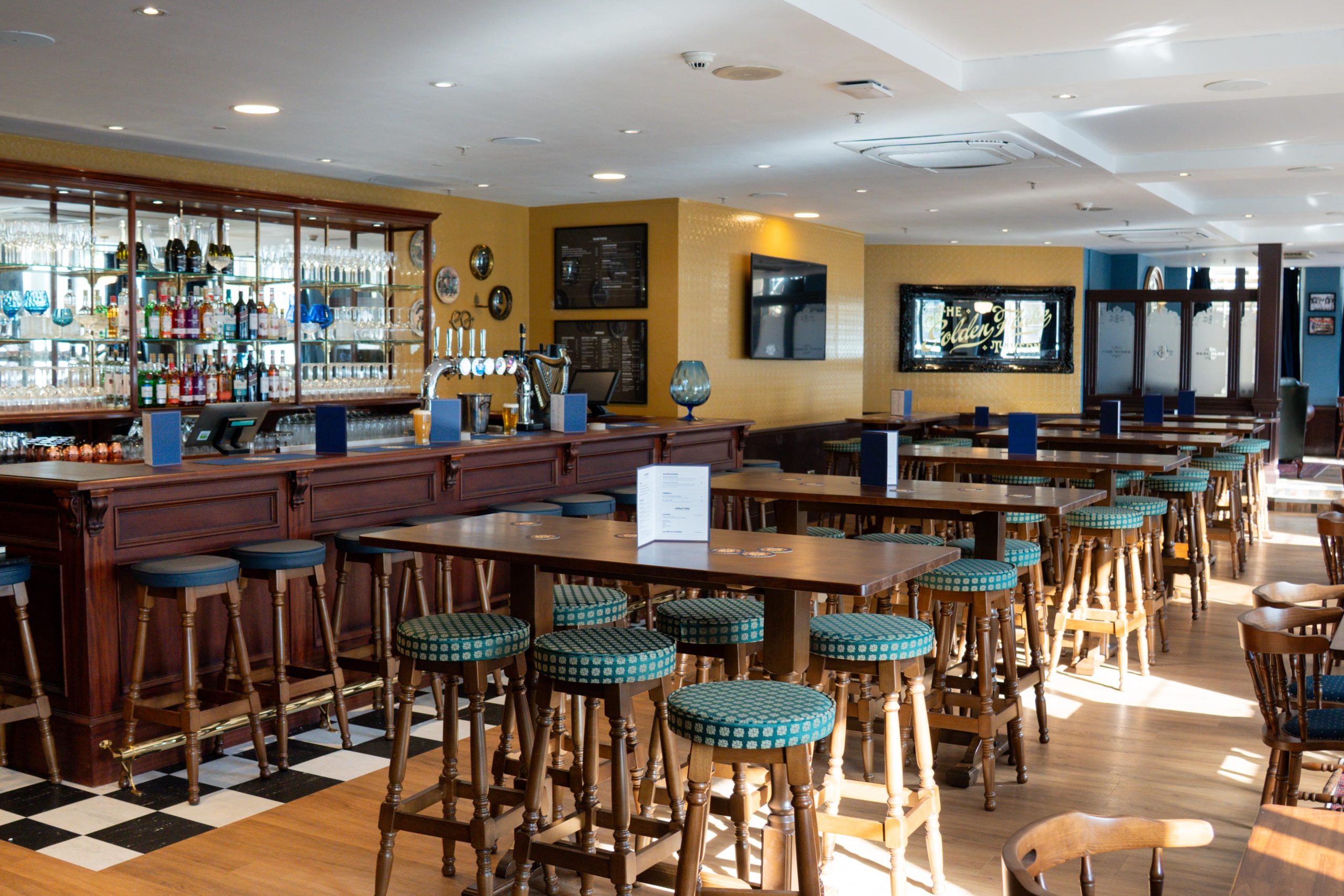 Pub-style room with bar on the left-hand wall and tall tables and tall stools lined across the room.