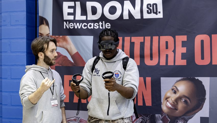 One person using a VR headset and another guiding them through the process in front of an Eldon Square branded banner.