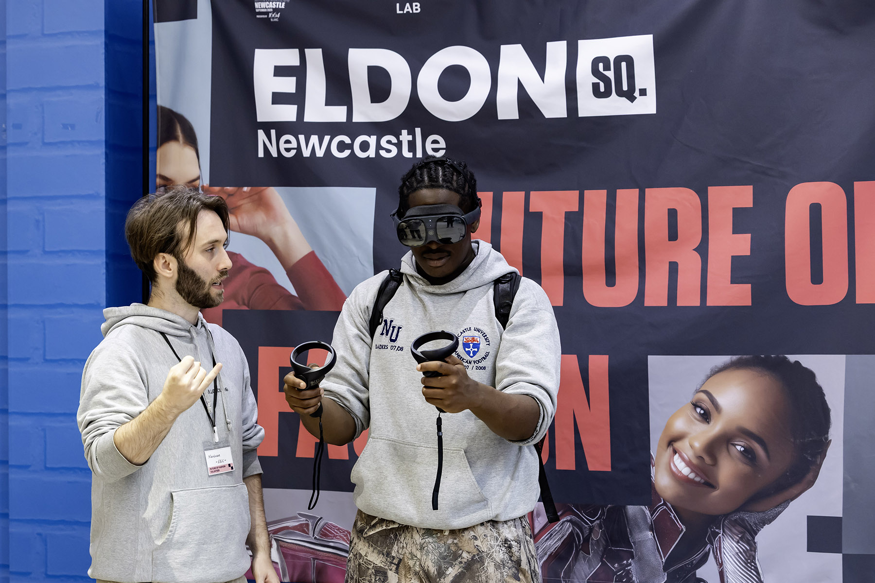 One person using a VR headset and another guiding them through the process in front of an Eldon Square branded banner.