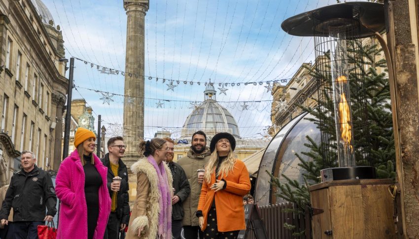 Group of friends in colourful clothing visiting a Christmas Market, smiling and laughing together.