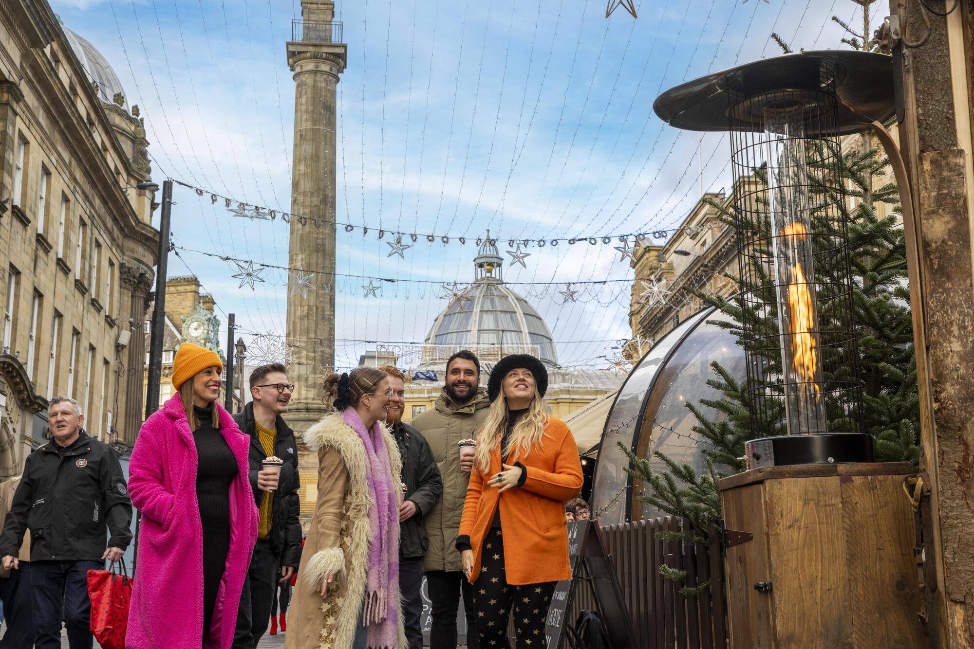 Group of friends in colourful clothing visiting a Christmas Market, smiling and laughing together.