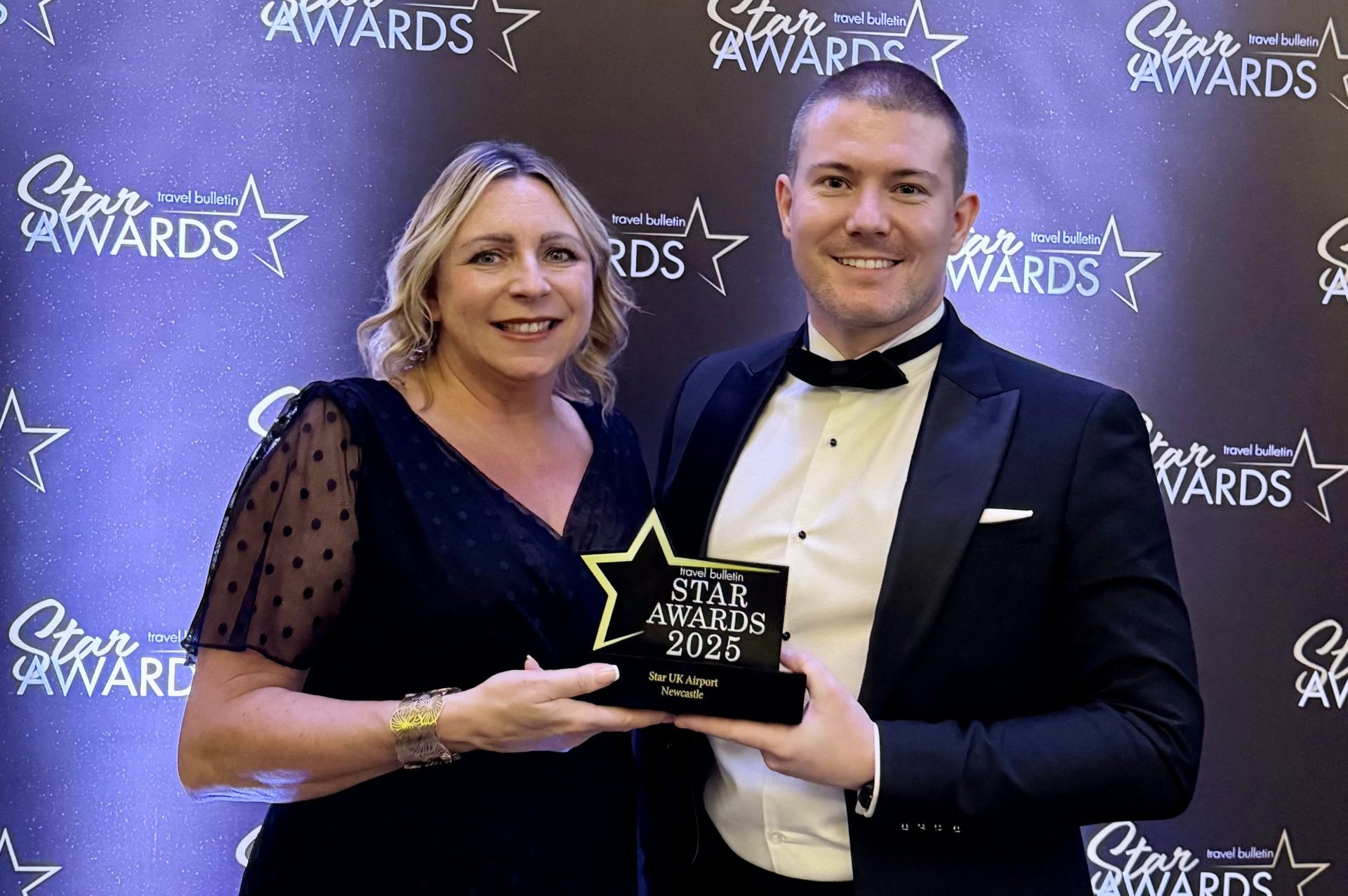 Laura and Chris holding up their award in front of the awards banner in black-tie attire.