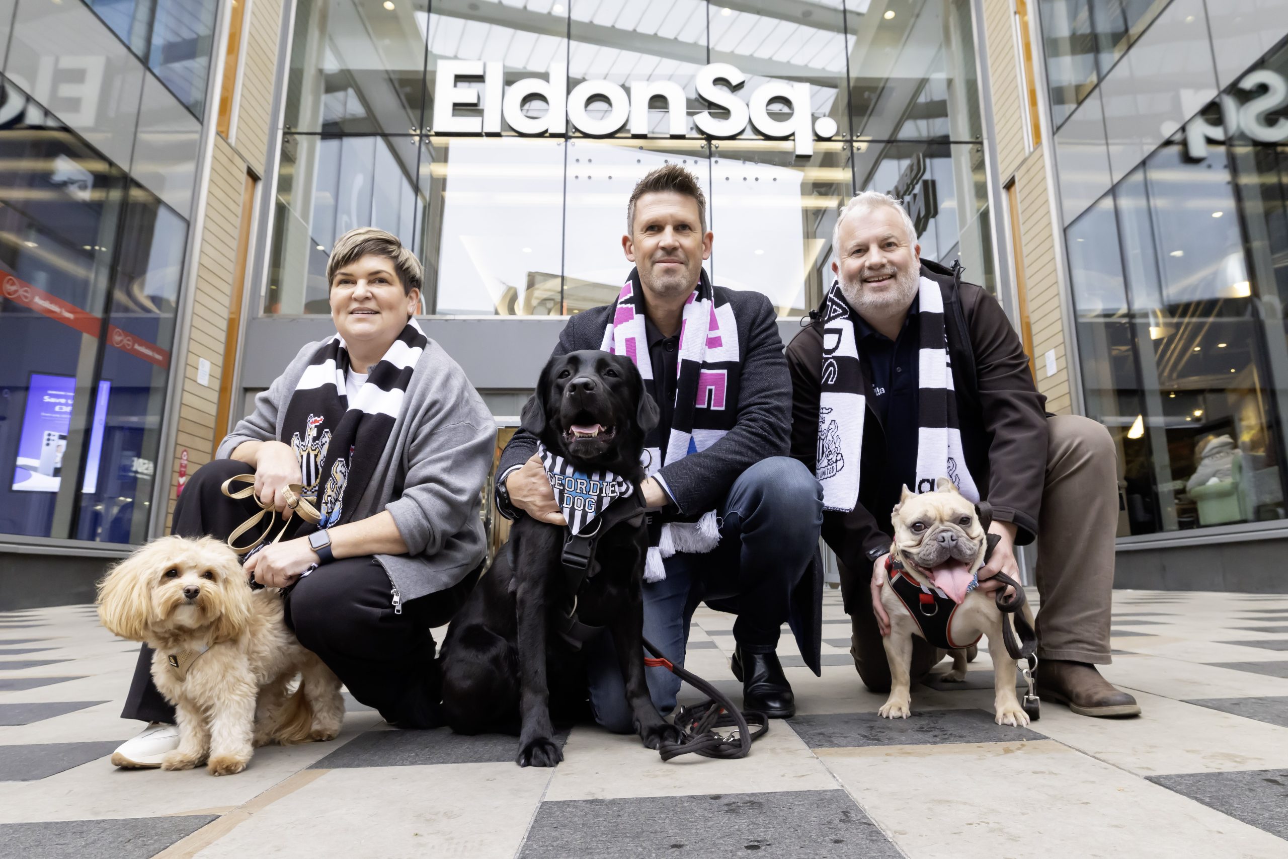 Three people wearing black and white striped NUFC scarves with three dogs.