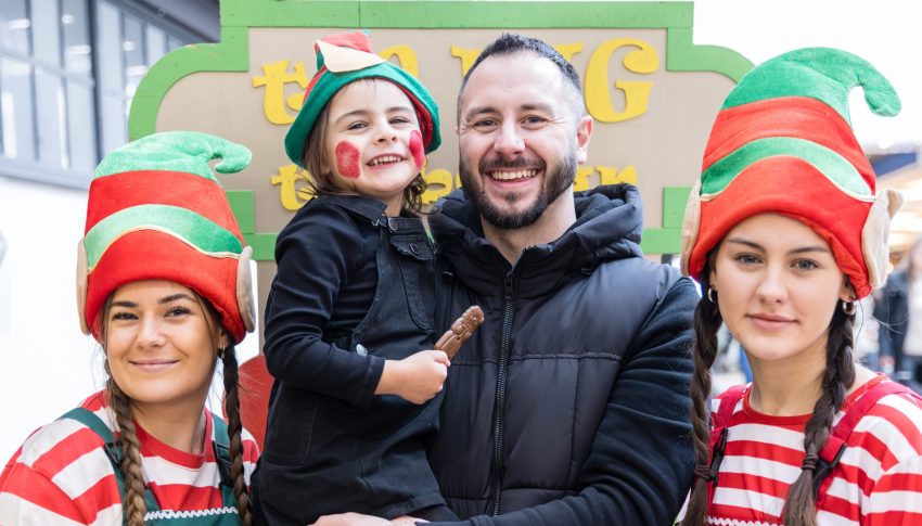 Father and child and two people dressed as Christmas elves smiling to camera.