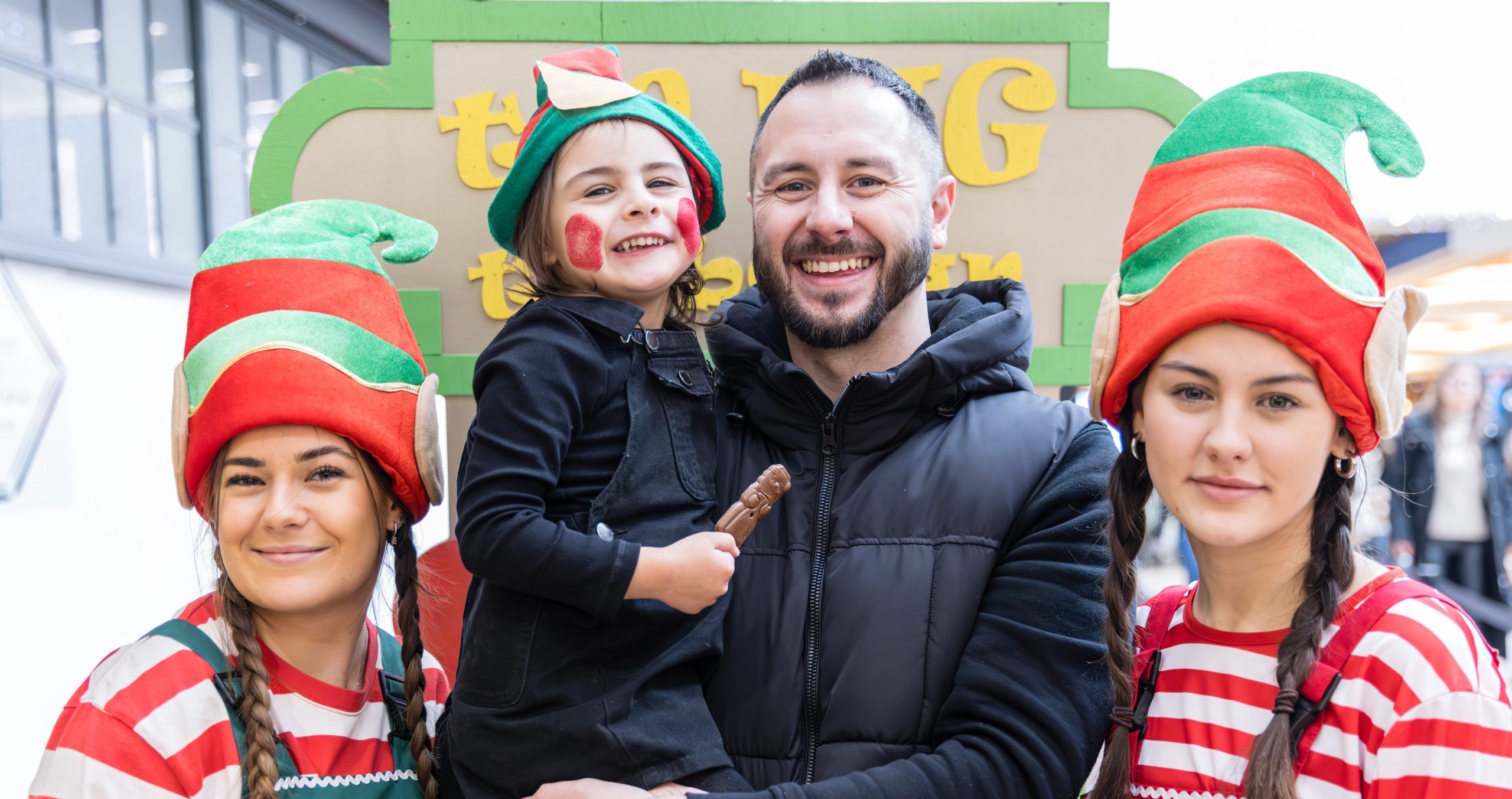 Father and child and two people dressed as Christmas elves smiling to camera.