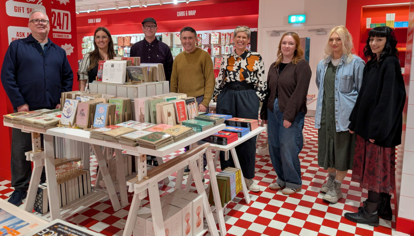 Group of NCG graduates stood in Fenwick with their Christmas cards displayed
