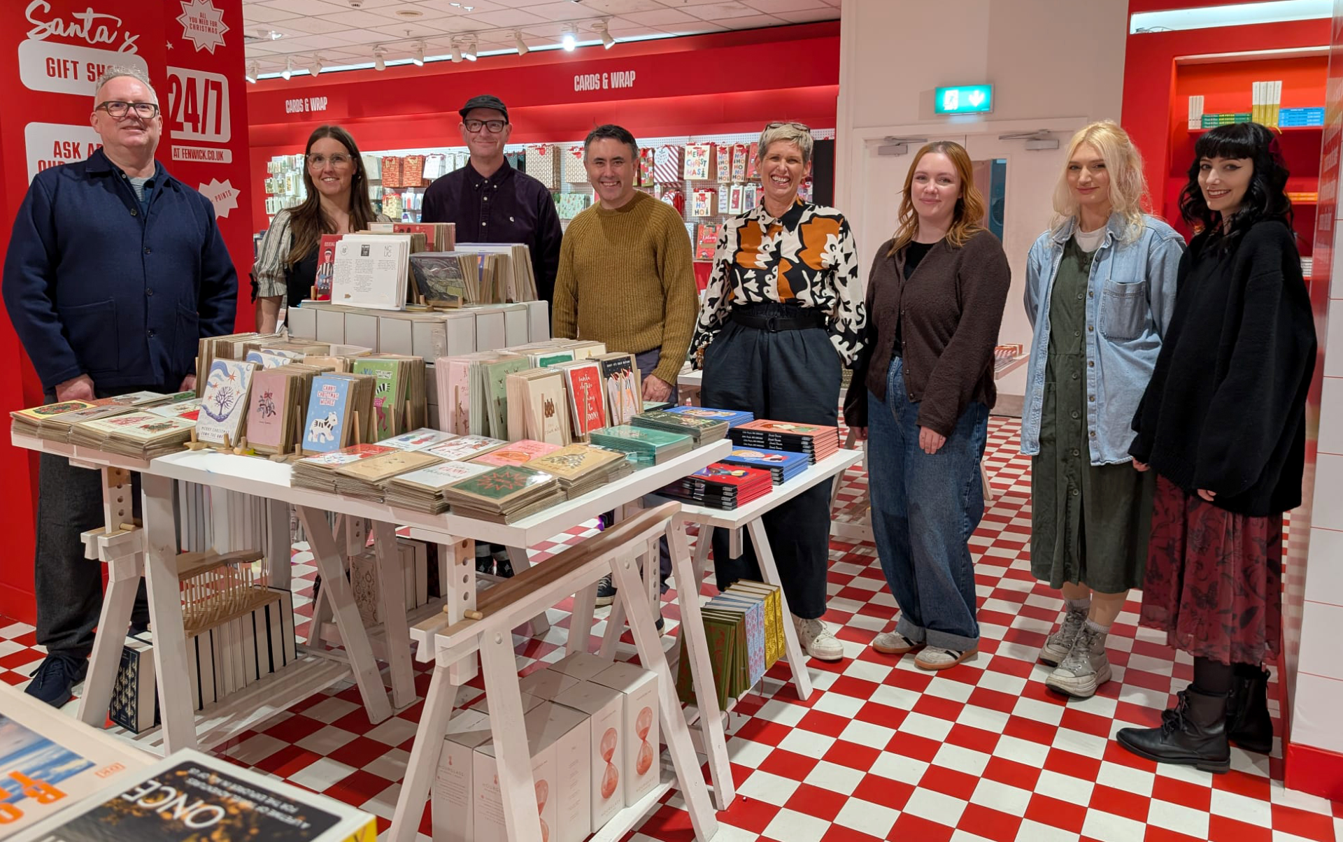 Group of NCG graduates stood in Fenwick with their Christmas cards displayed