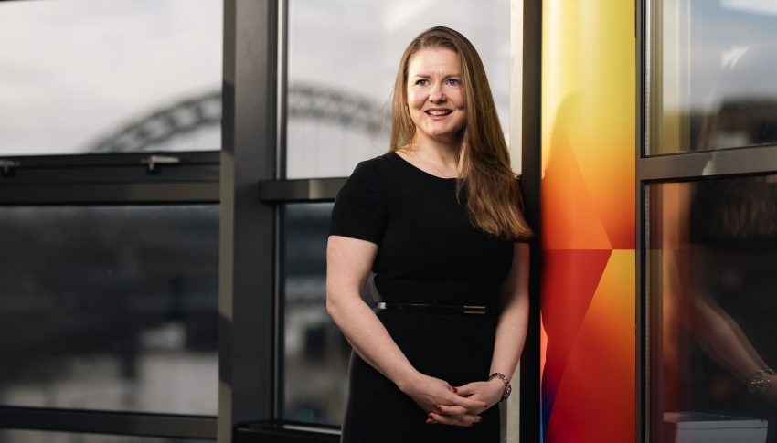 Louise Miller in a black dress in front of the Tyne Bridge.