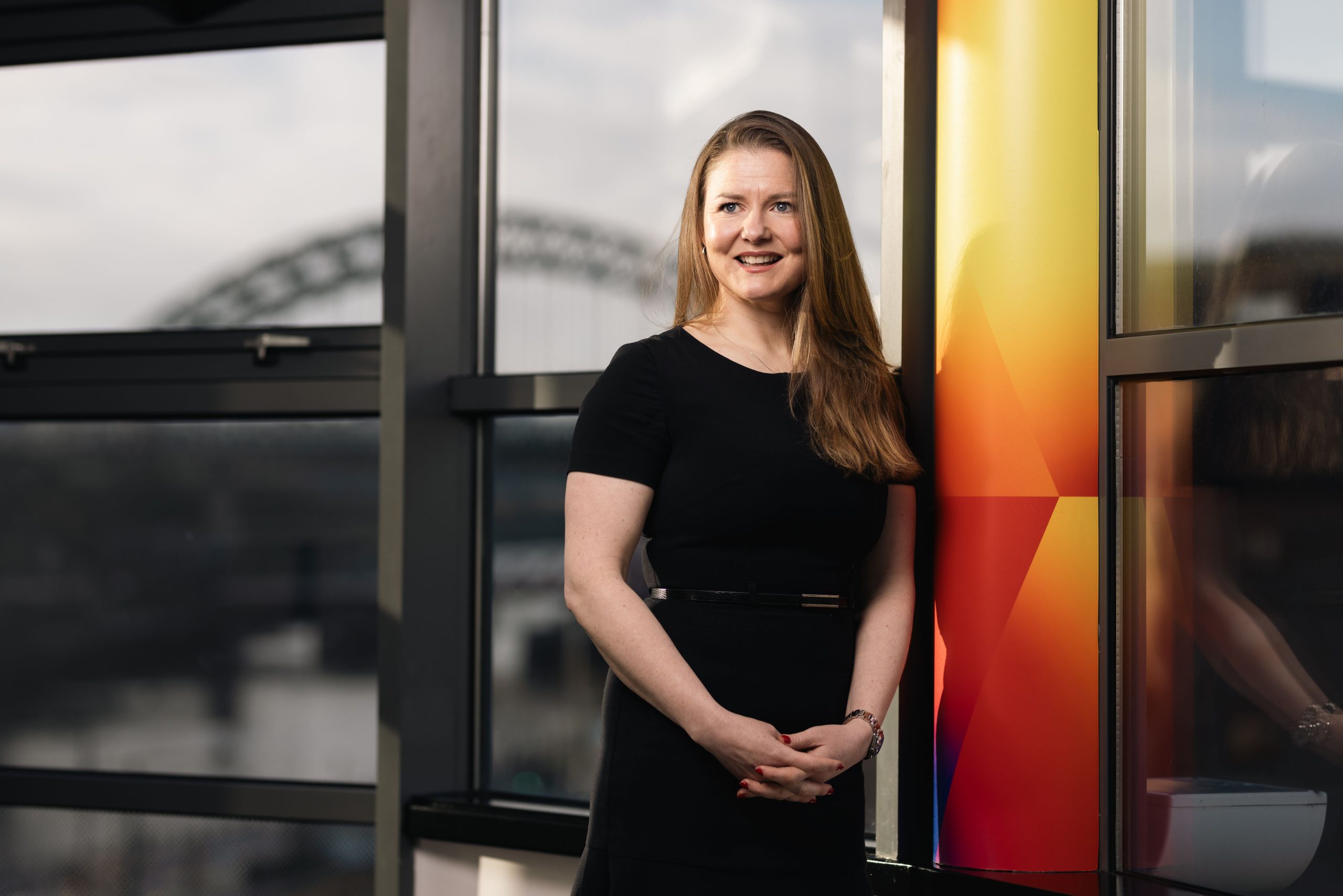 Louise Miller in a black dress in front of the Tyne Bridge.
