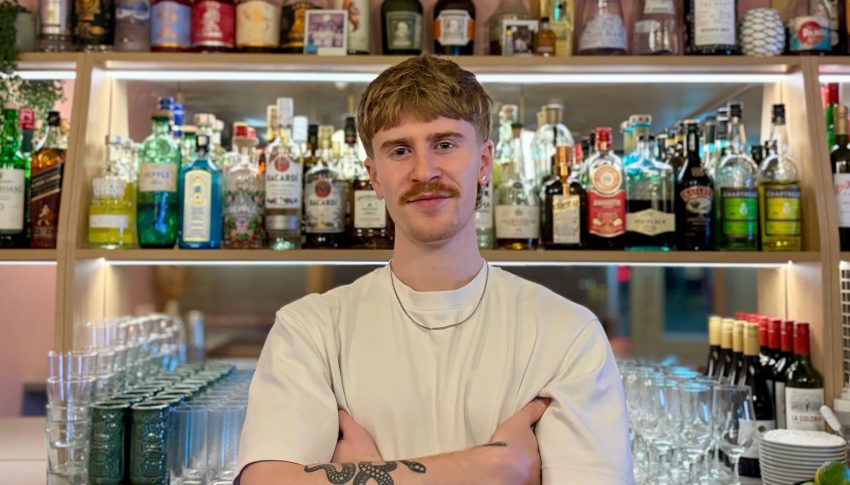 James Brown from Mother Mercy in a white T-shirt with bottles behind him.